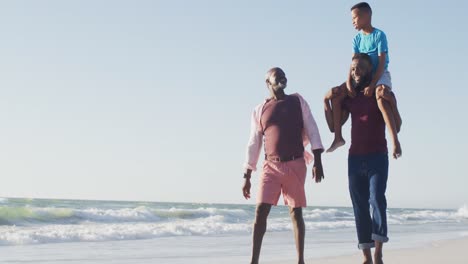 Video-De-Abuelo-Y-Padre-Afroamericanos-Cargando-A-Su-Hijo-En-Brazos-Y-Caminando-Por-La-Playa