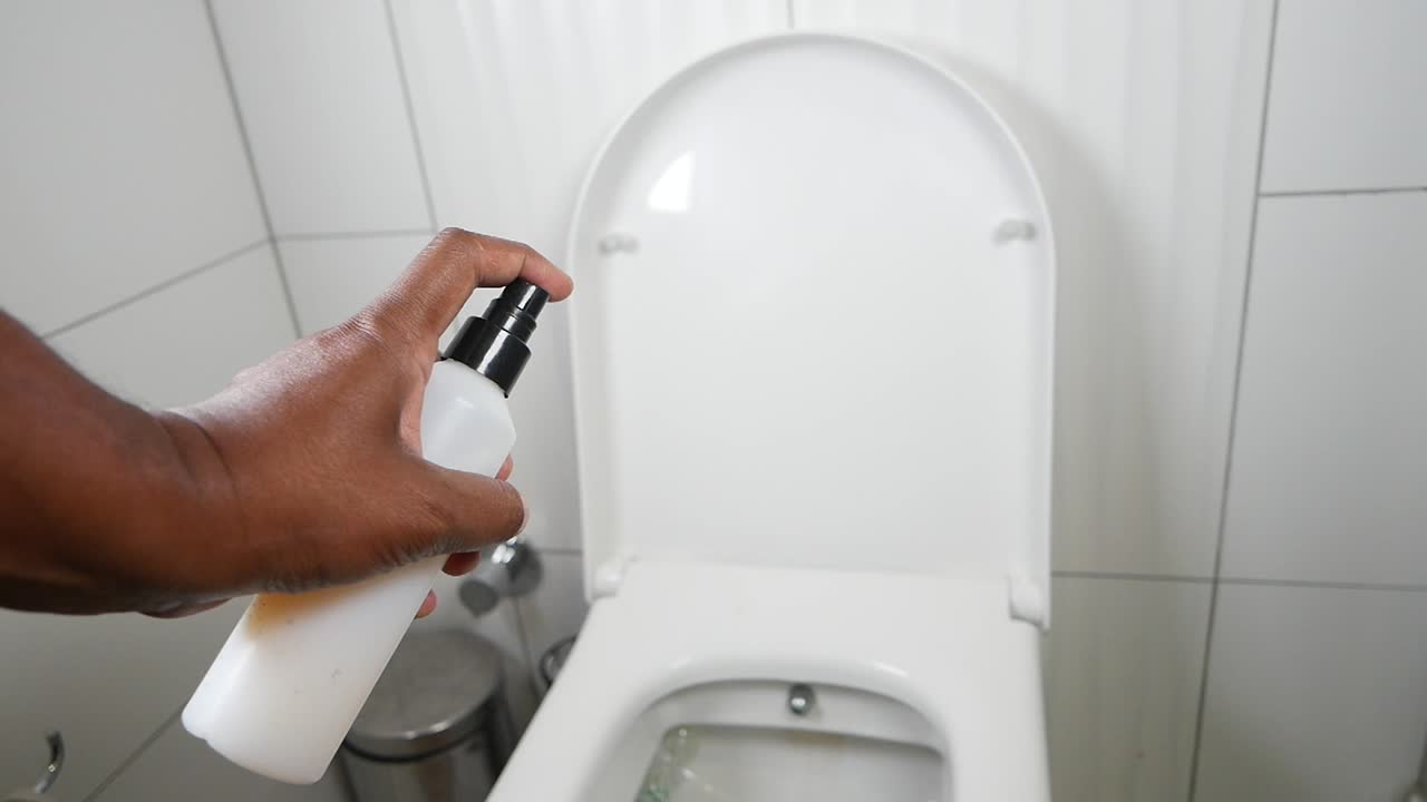 una persona rociando un inodoro con un producto de limpieza