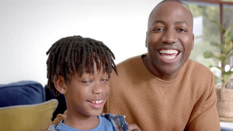 portrait of happy african american father and son embracing on sofa at home, slow motion