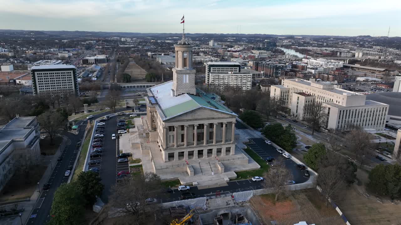 Ripresa aerea in avvicinamento del Campidoglio dello Stato del Tennessee a Nashville, che mostra la storica architettura governativa circondata da edifici e strade del centro in una giornata limpida. Bandiera americana sventolante in cima