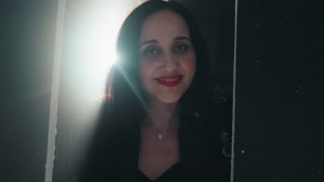 intimate close-up of a woman in black with red lipstick, smiling gently as the camera zooms in and light flares dramatically