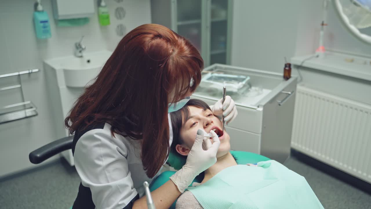Female dentist in dental office talking with female patient and preparing for treatment.