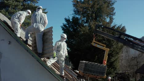 toma aérea dando vueltas alrededor de los techadores en trajes de materiales peligrosos para eliminar el amianto durante una renovación