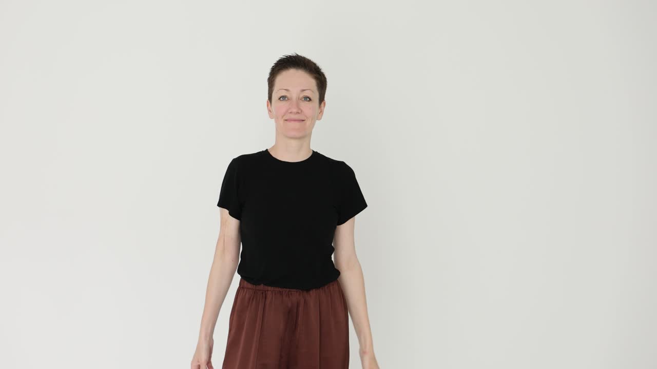 Una donna con una t-shirt nera e pantaloni marroni posa in uno studio