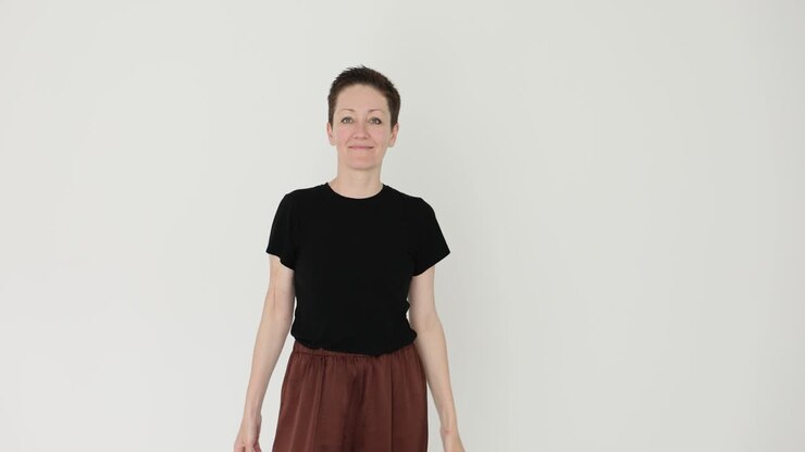En kvinde i en sort T-shirt og brune bukser poserer i et studie