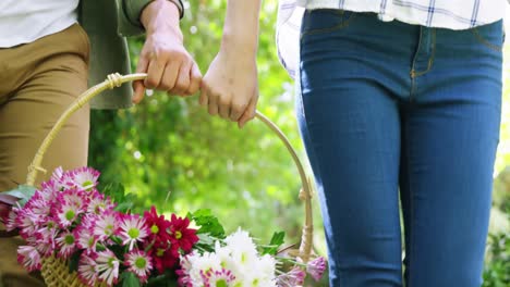 Mid-section-of-couple-holding-basket-full-of-flowers