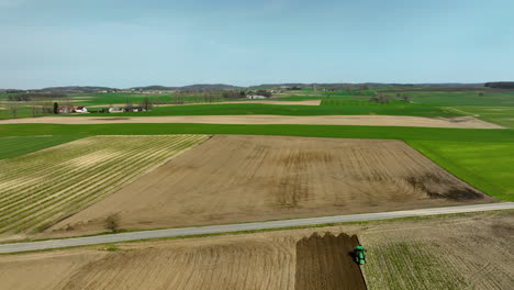 Aerial-shot-of-a-green-tractor-plowing-a-brown-field,-creating-neat-rows