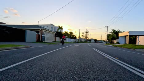 cyclist rides through suburban street at sunset