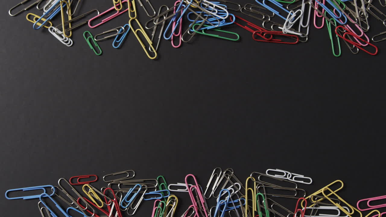 vista aérea de clips de papel de colores dispersos con espacio de copia en fondo negro, en cámara lenta