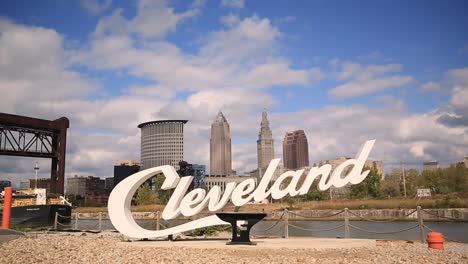 Cleveland,-Ohio-Skriptzeichen-An-Einem-Sonnigen-Tag-Mit-Wolken,-Die-An-Einem-Blauen-Himmel-Vorbeiziehen,-Und-Ein-Frachtschiff-Fährt-Vorbei