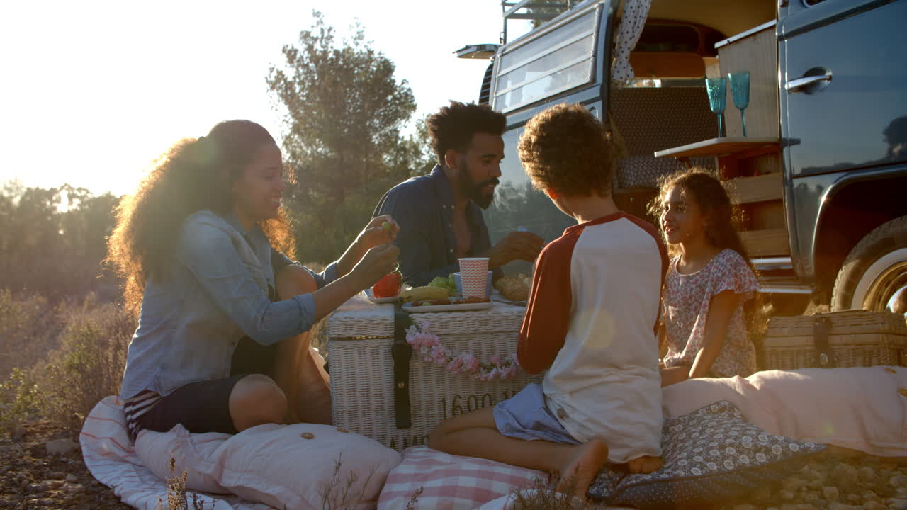 Famiglia che fa un picnic fuori dal loro camper al tramonto.