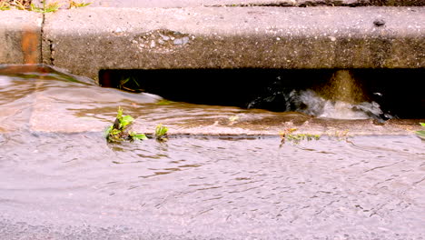 Frisches-Regenwasser-Fließt-über-Die-Dachrinne-Der-Betonstraße-In-Den-Regenabfluss,-Nahaufnahme