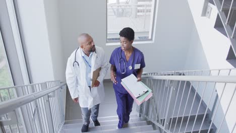 African-american-male-and-female-doctors-holding-clipboard-and-talking-at-hospital