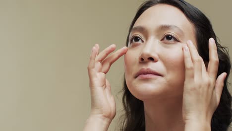 asian woman with dark hair touching her face on beige background with copy space, slow motion