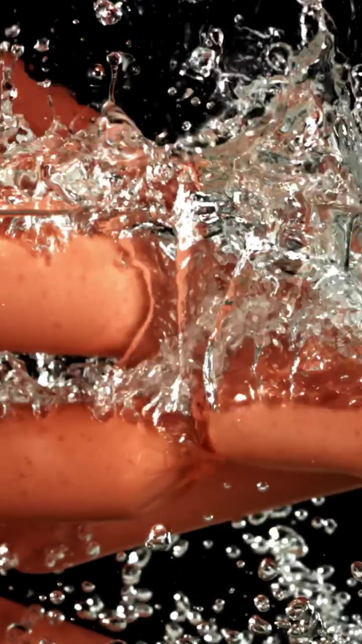 Due salsicce che cadono nell'acqua bollente con bolle al rallentatore