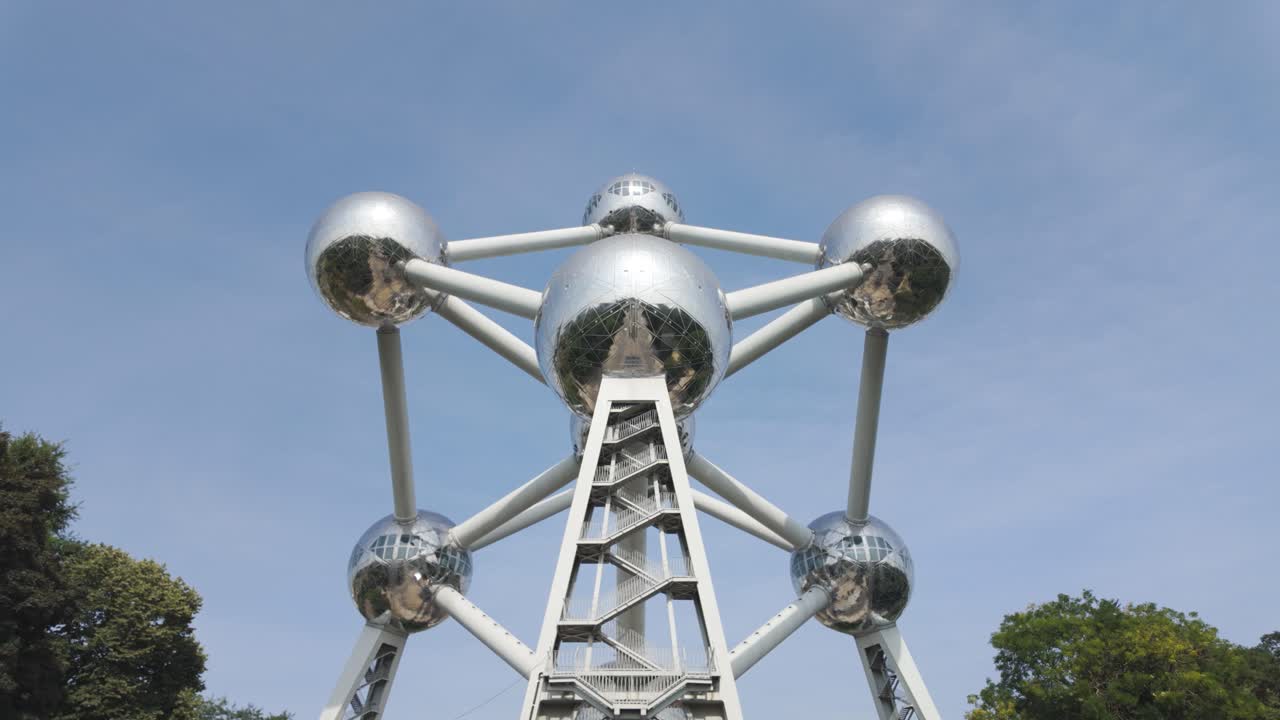 Low angle view of Atomium monument with blue sky in Brussels, Belgium, reflecting surrounding landscape. Tilt Down Shot