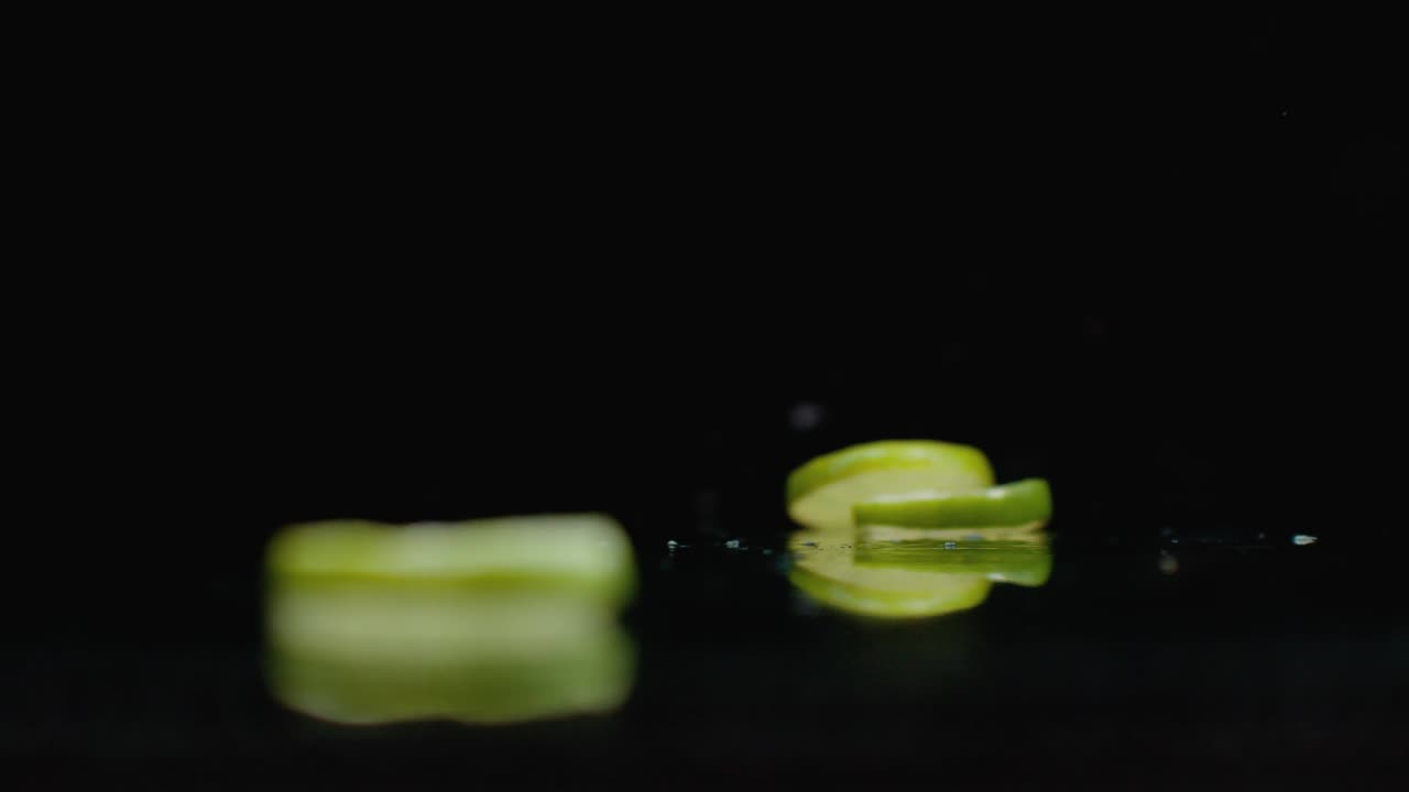 느린 움직임: 개진 라임 링은 어두운 배경의 유리 위에 물 어리와 함께 떨어집니다.