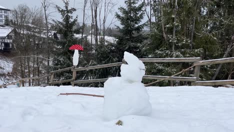 little snowman in front of wooden fence with snow and winter forest in the background