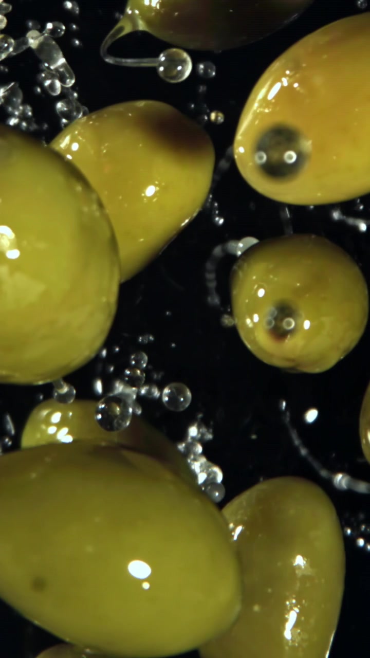 Olive verdi fresche che schizzano con gocce d'acqua su sfondo nero