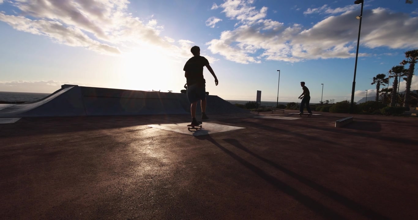 Sylwetka deskorolkarza odpychającego się o zachodzie słońca w skateparku