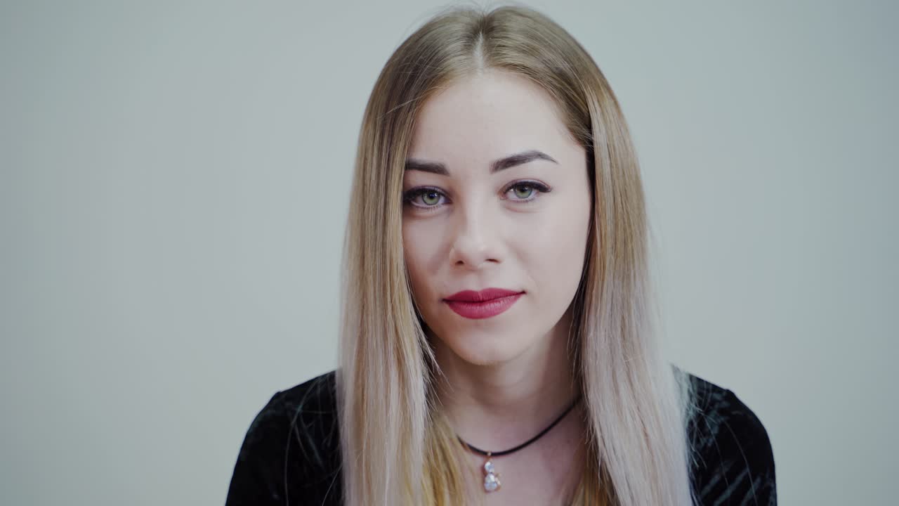 Portrait of a beautiful girl with perfect make-up. Blonde woman with long hair looking on camera and smiling on grey studio background.