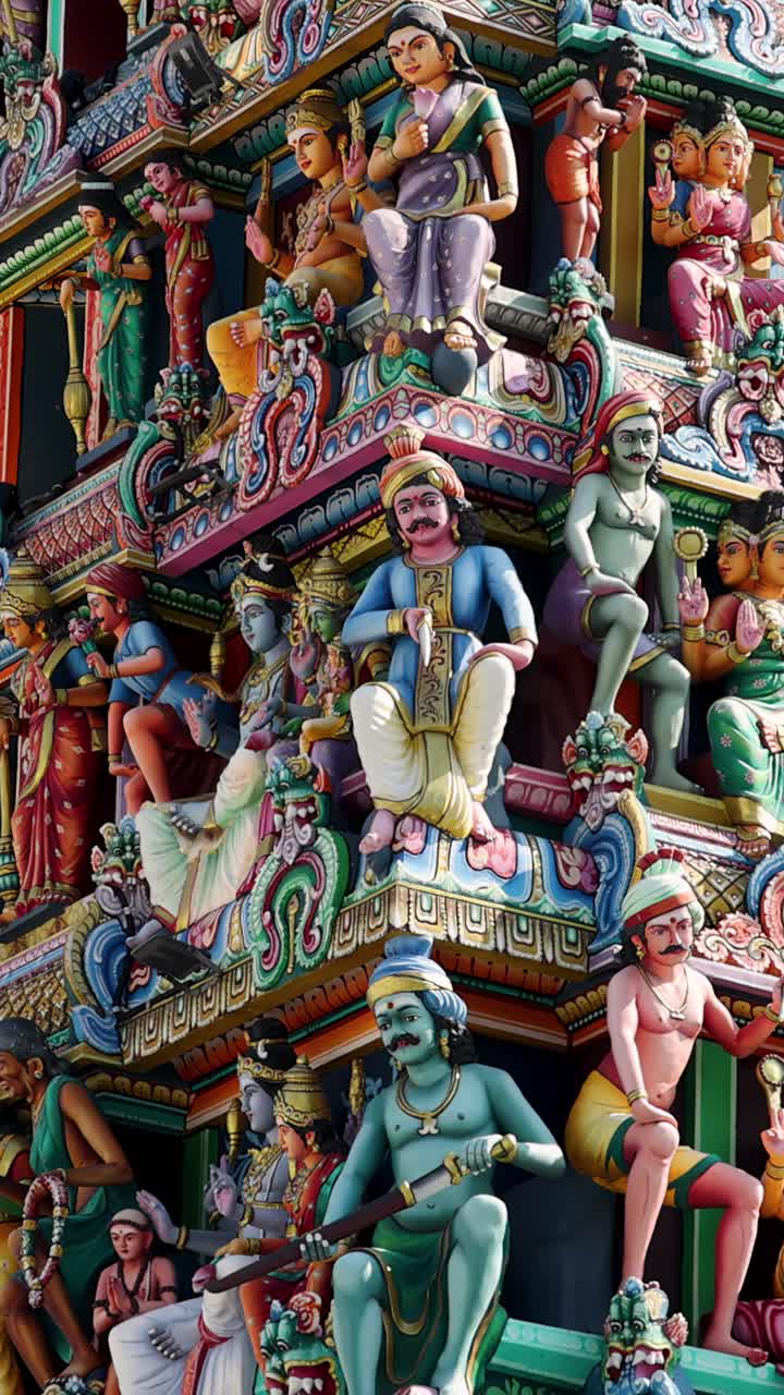 Panorámica vertical de cámara revela intrincadas estatuas y tallas de colores vivos en un gopuram de templo hindú bajo la luz natural del día en la Singapur urbana