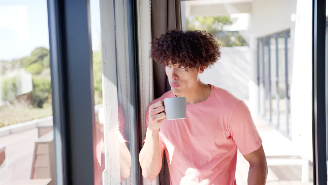 Holding coffee mug, man looking out window at home, relaxing