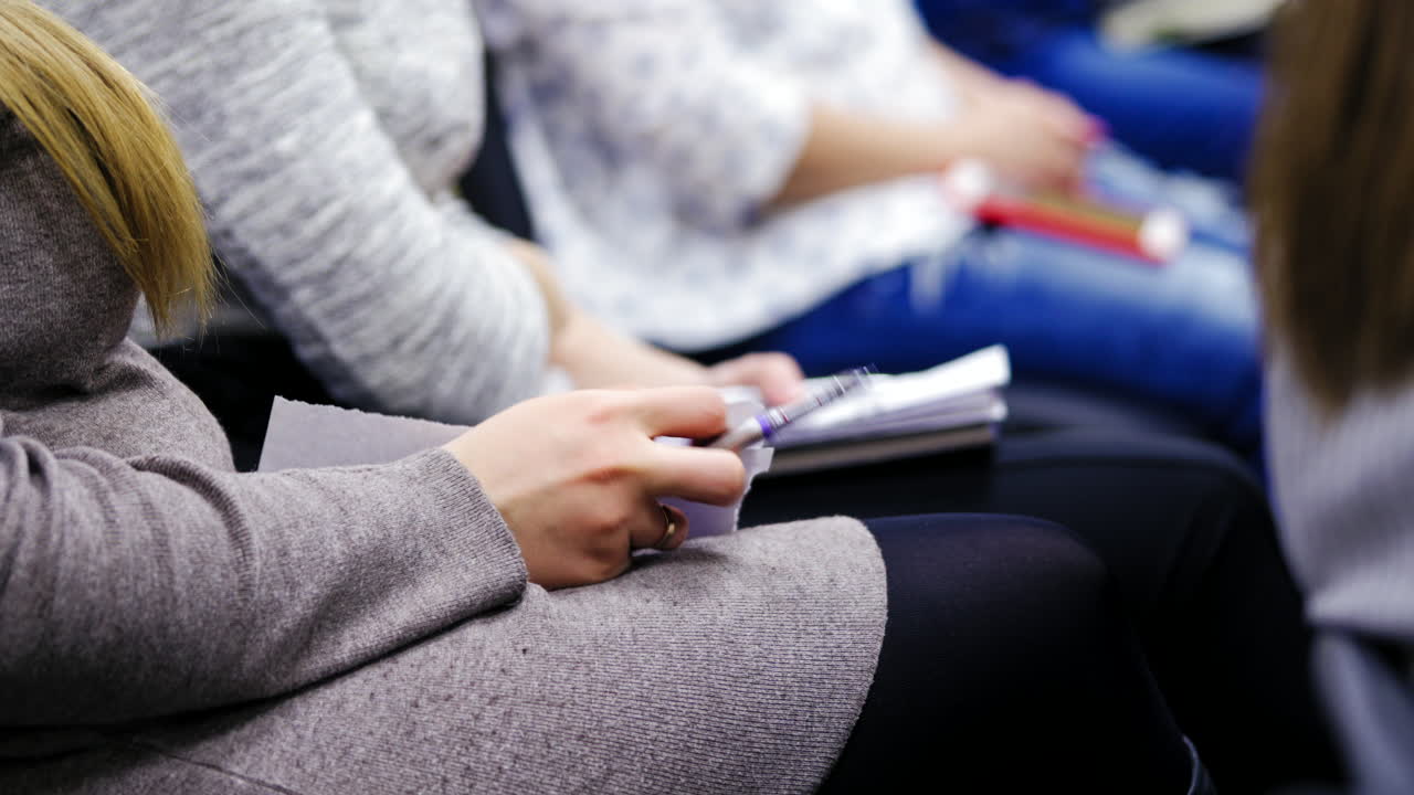 Close-up of female's hands holding pens and making notes at the conference. Woman is writing with a pen during the congress meeting.