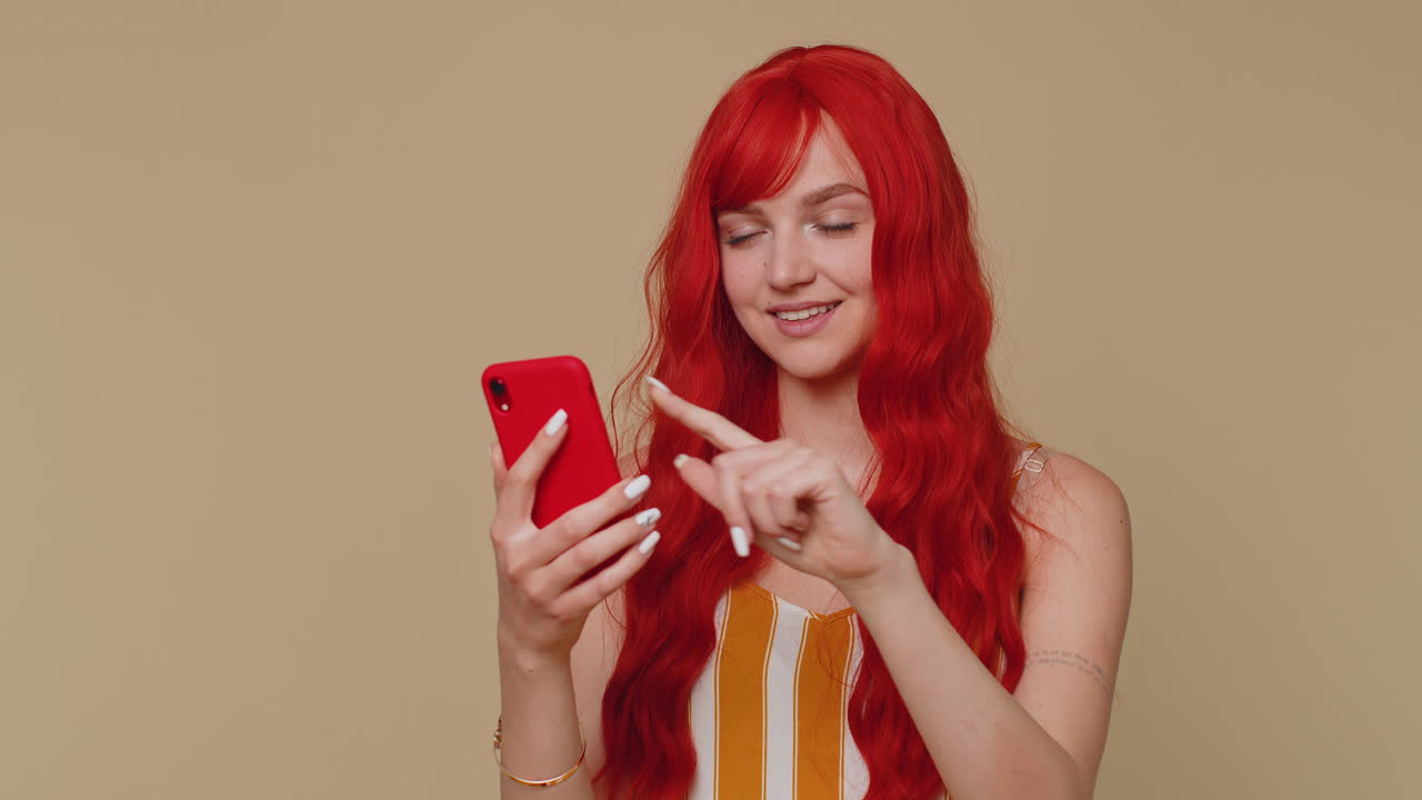 Ragazza dai capelli rossi che usa il cellulare che scrive post sul web che scrive SMS che naviga dipendenza dalle reti sociali