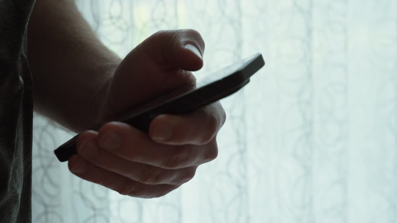 Close-up of a hand holding a smartphone and swiping on the screen in front of a bright window—ideal for TikTok scrolling, mobile addiction, doomscrolling, and digital lifestyle themes