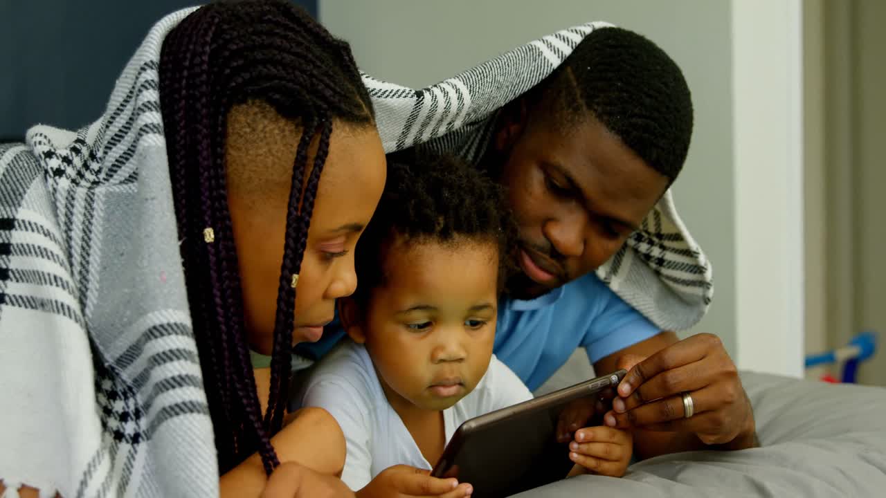 Vista laterale di una giovane famiglia di colore che usa un tablet digitale sul letto nella camera da letto di una casa confortevole 4k