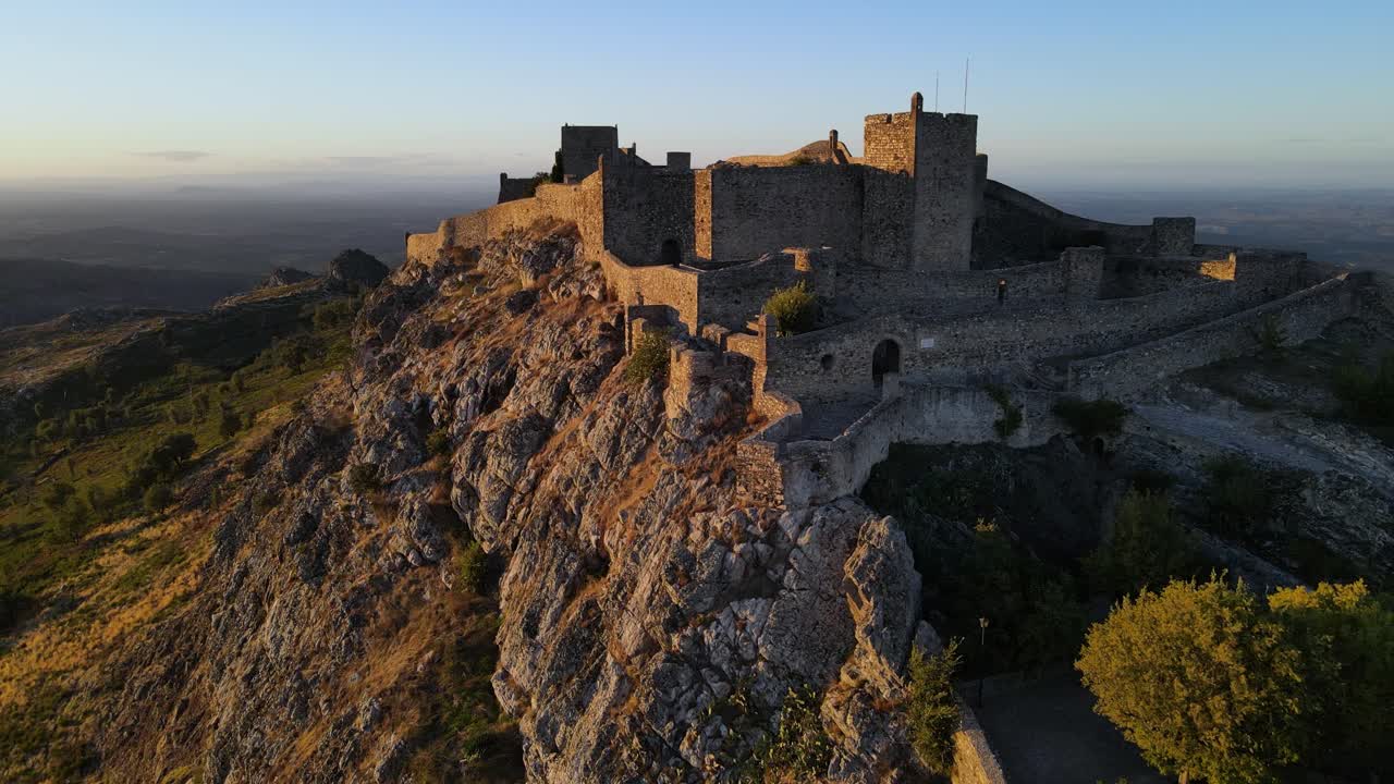 un dron pasa volando por los muros del castillo de marvao durante una puesta de sol dorada