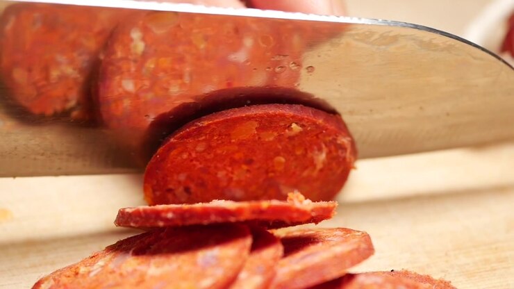 Primo piano di uno chef che affetta salsiccia chorizo su un tagliere di legno