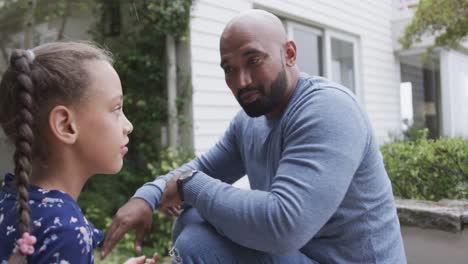 happy biracial father talking with daughter in garden, slow motion