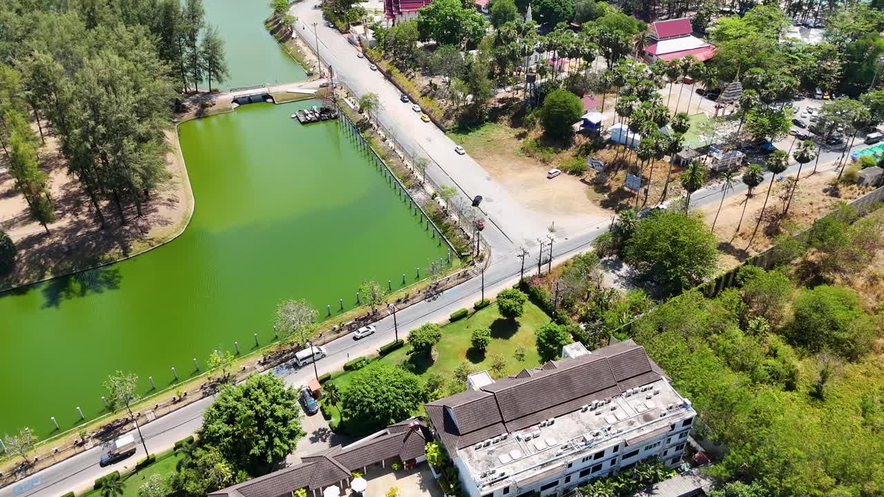 Drone footage captures a vibrant green lake and surrounding roads in Phuket, Thailand, under bright daylight, showcasing serene natural beauty