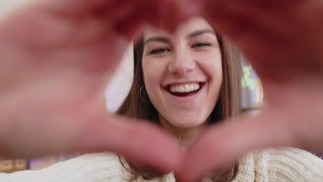 una joven feliz hace un símbolo de amor mostrando un corazón a la cámara para expresar sentimientos románticos