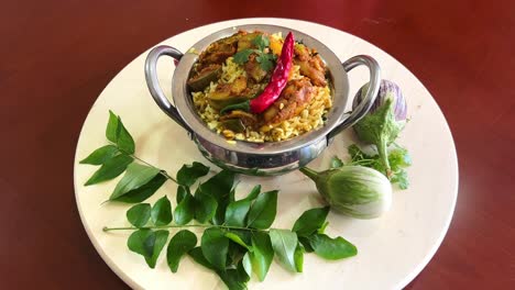 a bowl of brinjal biryani having herbs and spices and topped with a red chilli