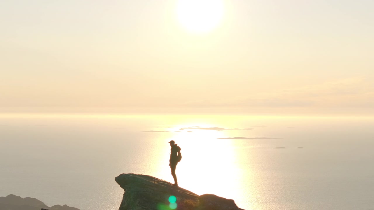 Escalador en la cima de una montaña panorámica en el Ártico noruego bajo el sol de medianoche; zoom de dron