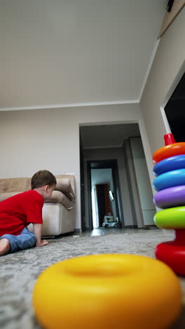 beautiful baby boy plays with his toys at home on the floor. black cat's muzzle appears smelling the toys. low angle view. vertical video.