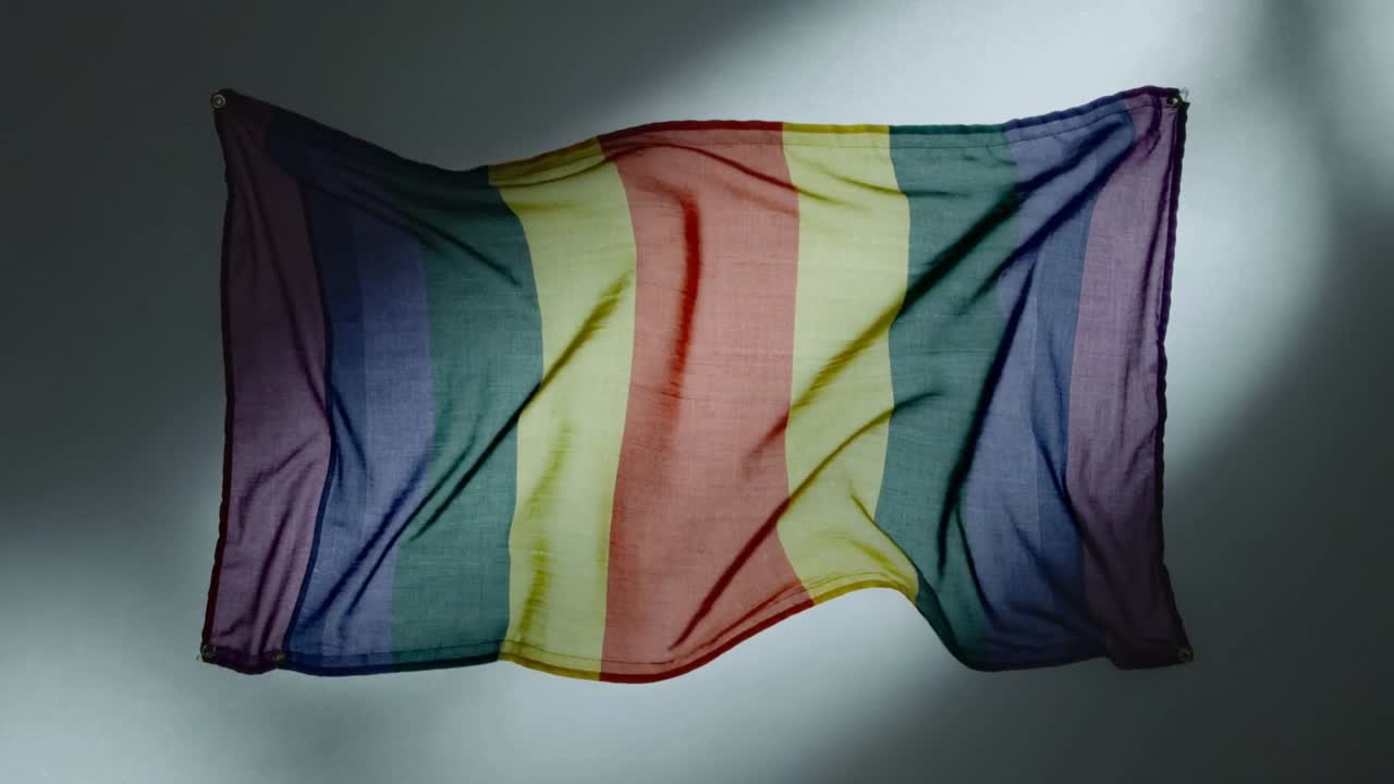 Bandiera arcobaleno che sventola per una brezza invisibile, mostrando increspature in studio, con occhielli e un riflettore.