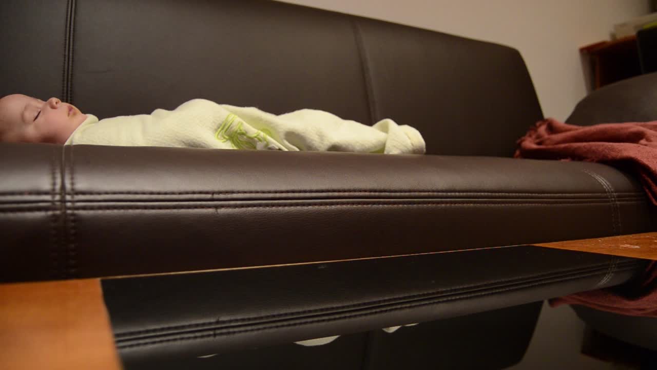 아기가 소파에서 자고 있는 동안 어머니는 커피 테이블을 청소하고 있습니다