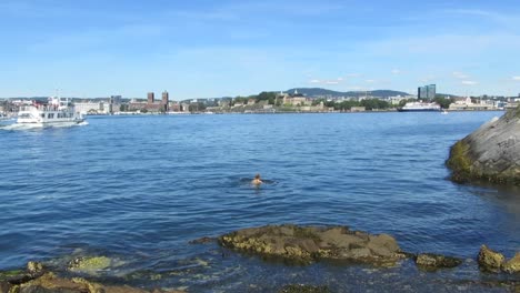 woman swimming in water outside oslo, norway, while ferry passes by