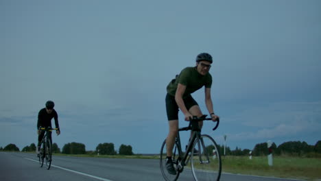 Dos-Ciclistas-Viajan-Por-La-Carretera-Por-La-Noche-Después-Del-Atardecer.-Temprano-En-La-Mañana-Entrenando-A-Ciclistas-Con-Cascos.