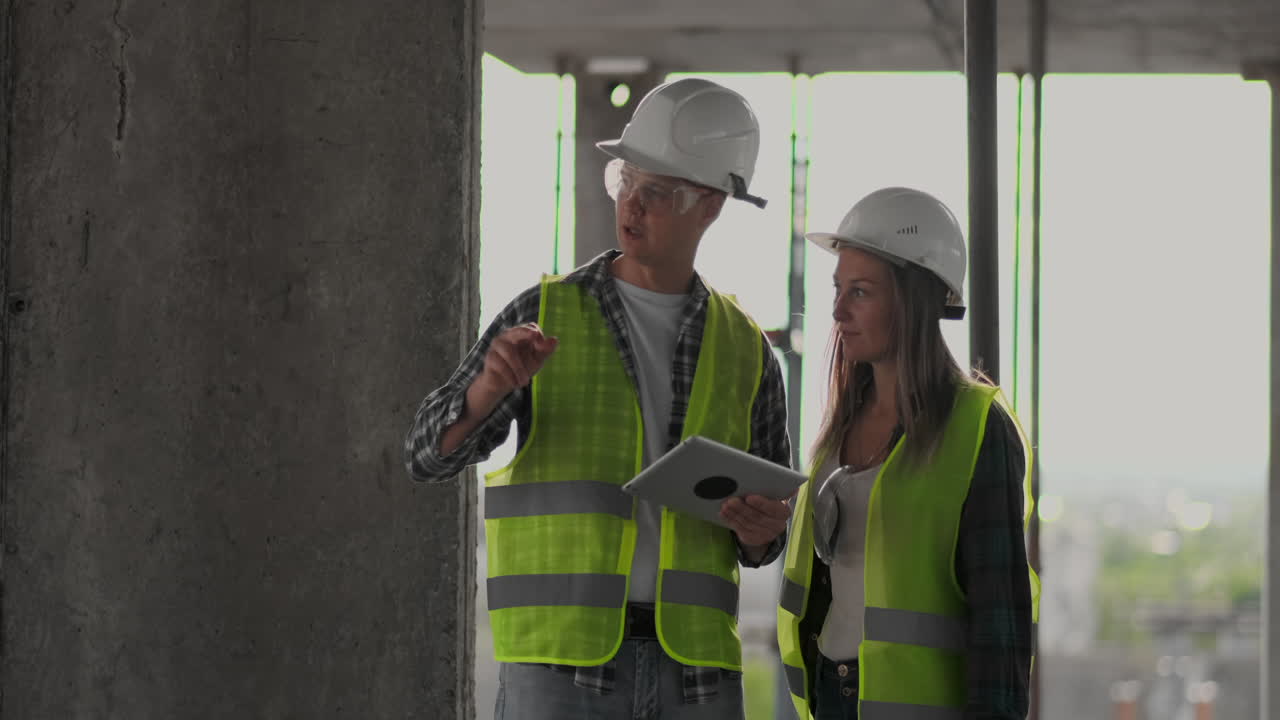 dos ingenieros un hombre y una mujer con cascos blancos con una tableta en el sitio de construcción condenan el plan de construcción del edificio