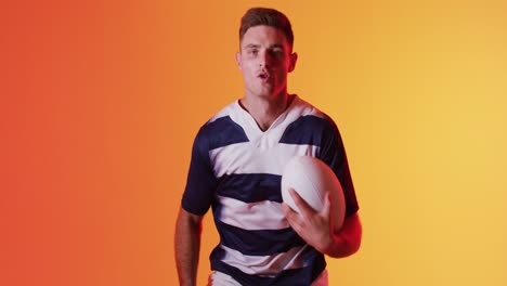 Portrait-of-caucasian-male-rugby-player-running-with-rugby-ball-over-orange-lighting