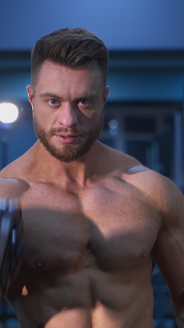 Fitness muscular man training his biceps in the gym. Handsome bodybuilder working hard at gym. Vertical video
