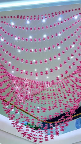 colorful paper flowers hanging indoors. bright pink paper flowers create a captivating display above a modern indoor space, illuminated by warm lights