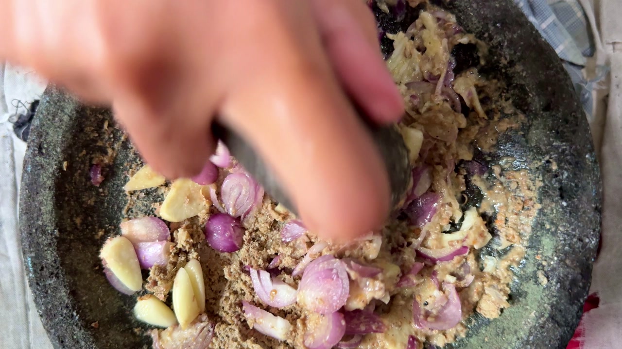 Traditional stone mortar used to grind spices and herbs. Close-up food preparation scene highlighting flavor, texture, and culinary culture.