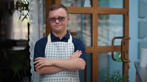 portrait of caucasian male waiter with down syndrome standing outside of a cafe.