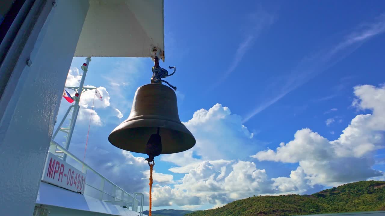 Brass ship's bell hanging on a ferry with a blue sky and islands in Philippines